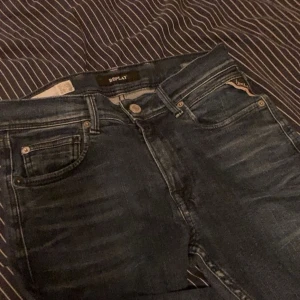 Mörkblå Replay jeans med klassisk look - Snygga mörkblå jeans från Replay med klassisk femficksdesign och diskreta slitningar framtill. Jeansen har tydliga kontrastsömmar och Replay-logga på bakfickan samt läderpatch i midjan. Perfekta för dig som gillar stilrena och tidlösa jeans. Kontakta mig om ni vill sänka priset!