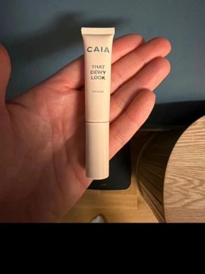 CAIA That Dewy Look Eye Gloss - Säljer en CAIA That Dewy Look Eye Gloss i en stilren beige tub. Ger en glansig finish till ögonlocken för en fräsch och modern look. Perfekt för dig som gillar glow och vill ha en enkel applicering med krämig konsistens.