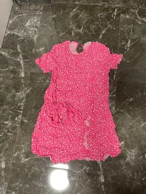 Rosa blommig kortklänning från Vila - Säljer en söt rosa kortklänning från Vila med vitt blommigt mönster. Klänningen har korta ärmar med volangdetaljer och en rund halsringning. Materialet är lätt och luftigt, perfekt för varmare dagar. Passar dig som gillar färgglada och romantiska plagg.