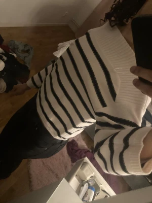 Vit och svart randig croppad tröja - Säljer en vit croppad tröja med svarta ränder och bred ribbad krage. Tröjan har offshoulder-design och långa ärmar, perfekt för dig som gillar en chill och trendig stil. Materialet känns mjukt och stickat, passar bra till jeans eller kjol.