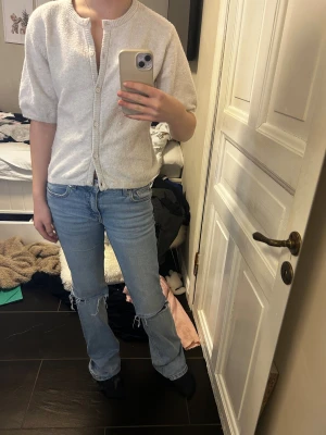 Vit kofta från Kappahl med knappar - Mysig vit kofta från Kappahl i storlek 170. Koftan har korta puffärmar, rund halsringning och stängs med knappar framtill. Materialet är mjukt och stickat, perfekt för lager-på-lager under kyliga dagar. Enkel och stilren design som funkar till jeans eller kjol.