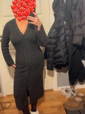 Mörkgrå stickad långklänning V-ringad - Otroligt fin stickad klänning, endast använd 1 gång!  Knapparna går att öppna och kan användas som kofta. Storlek xs men passar mig som i vanliga fall är S. Är 164 och den går till mina anklar