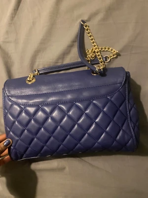  handväska från Love Moschino - Säljer en snygg blå handväska från Love Moschino med quiltad design och guldfärgade kedjedetaljer. Köpte för 2000kr