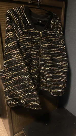 Svart kofta med glittriga ränder från H&M - Säljer en svart kofta från H&M i storlek M med glittriga, flerfärgade ränder. Koftan har dragkedja framtill och ribbade muddar vid hals och ärmslut. Materialet är stickat och har en mysig, lite fluffig känsla. Perfekt för dig som gillar att sticka ut med detaljer, samt lite festlig.