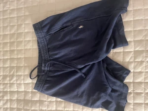 Mörkblå shorts från Polo Ralph Lauren - Säljer ett par mörkblå shorts från Polo Ralph Lauren med klassisk logga broderad framtill. De har elastisk midja med snörning och är gjorda i mjuk bomull, perfekt för chill dagar. Passformen är loose och de har en enkel, stilren design.