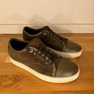 Lanvin skor - Snygga sneakers från Lanvin i olivgrönt mocka med detaljer i grönt skinn på tån och vita gummisulor. Skorna har rund tå, snörning och metallöglor. Perfekt för dig som gillar stilrena och exklusiva sneakers med en cool touch. Perfekt nu när vi börjar gå in i mörkare väder.