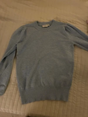 Ljusblå stickad tröja Saint Tropez XS - Säljer en ljusblå stickad tröja från Saint Tropez i storlek XS. Tröjan har rund hals, ribbade muddar och långa ärmar med lätt puff vid axlarna för en snygg touch. Perfekt för dig som gillar enkel men stilren design.