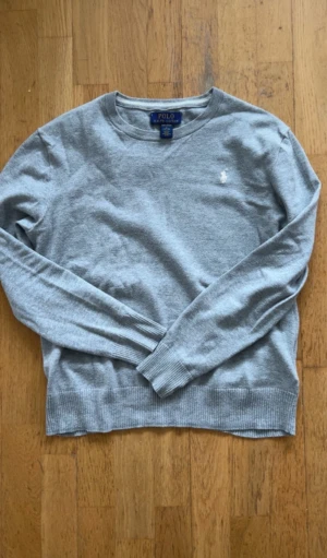 Grå tröja från Polo Ralph Lauren - Snygg grå tröja från Polo Ralph Lauren i mjuk pima bomull. Klassisk rund hals och långärmad modell med ribbade muddar och nederkant. Diskret broderad logga på bröstet. Perfekt för en chill och stilren look.