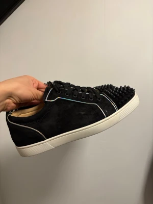 Christian Louboutin svarta sneakers med nitar - Svarta sneakers från Christian Louboutin i mocka med vita detaljer och holografisk piping.  Skorna är äkta och i topp skick. Endast skorna medföljer därav priset! ✅