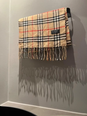 Burberry halsduk - Säljer denna stilrena halsduken från märket Burberry, halsduken är väl använd, skicket på den är 8/10✅ mått 30cm bred längd runt 150cm. Skickas inom 24h✅pm vid frågor