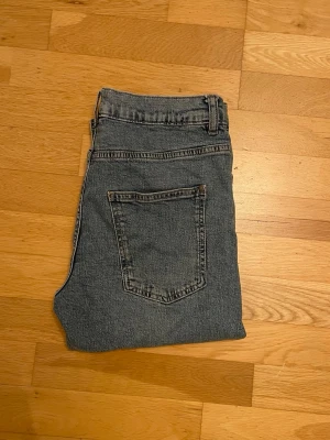Grå straight jeans med fem fickor - Snygga grå jeans med klassisk femficksdesign och rak passform. Jeansen har bälteshällor, knapp och dragkedja framtill samt en enkel bakficka. Materialet är slitstarkt jeans och färgen är en neutral grå ton som passar till det mesta.