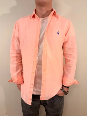 Rosa linneskjorta från Ralph Lauren - En stilren linneskjorta från Ralph Lauren. Second hand men i bra skick ✨ Tvättad och struken – redo att användas direkt.  Perfekt för vår/sommar, funkar både upplätt och casual. Riktigt snygg på stranden eller med ett par vita jeans.  Lite urtvättad och står slim fit men snarare regular.   Storlek 👔: M Nypris 💰: ca 1 300 kr