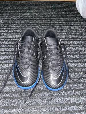 Nike Mercurial futsalskor - Nike Mercurial svarta futsalskor med blå sula, blåa och vita detaljer och svarta snören. De är knappt använda och är i storlek 35.