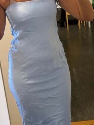 Ljusblå satin klänning från Bershka - Säljer en ljusblå, figurnära klänning från Bershka i satinliknande material. Klänningen är axelbandslös och har en slät, enkel design som ger en stilren look. Perfekt för dig som gillar minimalistisk stil och mjuka färger.