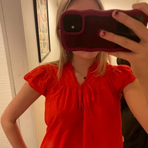 Röd blus med knytband - Säljer en superfin röd blus med korta ärmar och knytband vid halsen. Perfekt för både vardag och fest! Blusen har en lös passform. Passar perfekt till jeans eller kjol för en snygg look.