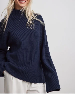 Marinblå stickad polotröja - Säljer en marinblå stickad polotröja med hög hals och breda, långa ärmar. Tröjan har en loose passform och är tillverkad i ett grovstickat material som känns både mjukt och varmt. Perfekt för dig som gillar en chill och stilren look.