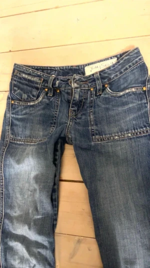 Teddy smith Low Rise jeans  - Säljer ett par blå jeansbyxor från Teddy Smith som har snygga detaljerade bakfickor med knappar. Klassisk femficksmodell och normal passform. Perfekta till sneakers eller boots för en avslappnad look.