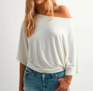 Vit offshoulder topp med trekvartsärm - Säljer en vit offshoulder topp med avslappnad passform och trekvartsärmar. Toppen har en mjuk och slät yta, är lätt croppad och sitter snyggt över ena axeln. Perfekt för dig som gillar en stilren och enkel look. Aldrig använt 