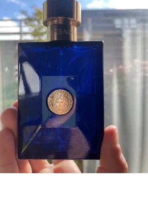 Stilren blå Versace parfym - Snygg parfymflaska från Versace i djupblått med gulddetalj. Perfekt för dig som vill ha en lyxig känsla i din samling. Volym och ingredienser syns ej på bilden.