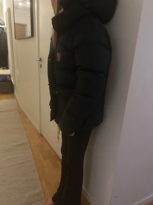 Svart Fjällräven Expedition dunjacka - Säljer en svart Fjällräven Expedition dunjacka med huva och gula snören. Jackan har puffad design, tryckknappar och klassisk Fjällräven-logga på bröstet. Perfekt för kalla vinterdagar och har en riktigt schysst streetstil. Fodrad med dun för extra värme. Ny skick knappt använd ska även läggas till.