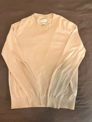 Beige bomullströja These Glory Days - Snygg beige tröja från These Glory Days i mjuk superior bomull. Rund halsringning och långa ärmar med ribbade muddar vid ärmslut och nederkant. Perfekt för dig som gillar stilrena och enkla plagg med skön passform.