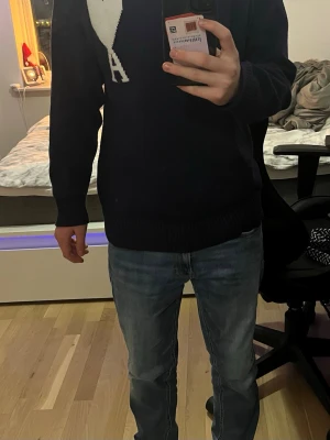 Mörkblå stickad tröja från Ami - Säljer en mörkblå stickad tröja från Ami med ett stort vitt hjärta och bokstaven A på bröstet. Tröjan har rund hals, ribbade muddar och lång ärm. Perfekt för dig som gillar stilrena detaljer och vill ha något som sticker ut lite extra. Skicket är mycket bra då den är så gott som ny. Har använt en gång endast 