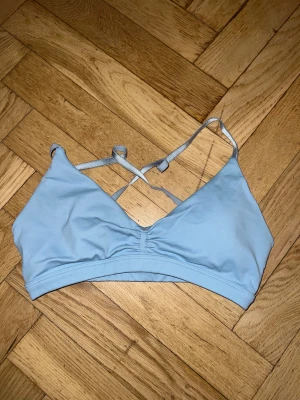 Ljusblå sport-bh från Relode - Säljer en ljusblå seamless sport-bh från Relode med öppen rygg och justerbara band. Bh:n har en snygg omlott-design och lätt rynkning framtill. Perfekt för träning och har en mjuk, stretchig känsla i syntetmaterial.