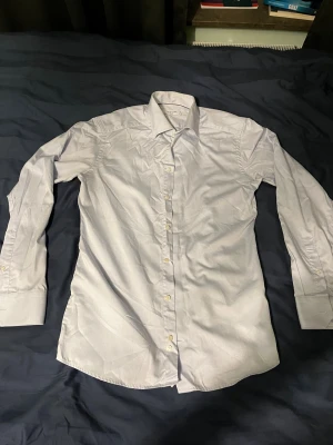 Slim vit skjorta från Eton - Snygg vit skjorta från Eton i slim fit med klassisk krage och långa ärmar. Skjortan har knappar framtill och är tillverkad i bomull, vilket gör den skön och stilren. Perfekt för dig som gillar en clean och fräsch look.