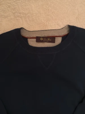 Loro Piana tröja - Snygg blå tröja från Loro Piana med rund hals och ribbade muddar. Tröjan har diskreta kontrastdetaljer vid hals och ärmslut. Tillverkad i mjuk kashmir och silke, perfekt för dig som gillar klassisk och stilren look. Helt ny bara att lappen halvt är av. Kostar runt 10000kr från butik. 