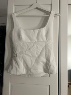 Vit linnetopp med rosett och öppen rygg - Säljer en vit linnetopp med breda axelband och snygg fyrkantig halsringning. Toppen har en stor rosett och en öppen ryggdetalj som gör den extra unik. Materialet är slätt och har en lätt struktur. Perfekt för dig som gillar stilrena och trendiga plagg. Har en dragkedja på sidan och ganska stor i storlek 