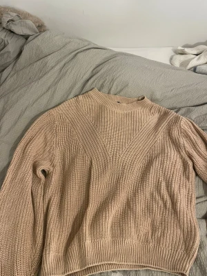Beige stickad tröja från H&M Divided - Säljer en beige stickad tröja från H&M Divided i storlek M. Tröjan har en högre rund hals och ett snyggt ribbat mönster som ger en cool struktur. Perfekt för att hålla sig varm under kyliga dagar och passar till många olika stilar.