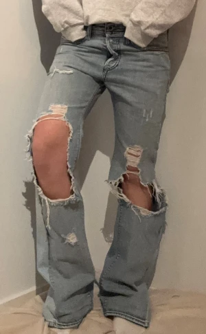 Ljusblå ripped jeans med bootcut - Säljer ett par ljusblå jeans från Levi's med rejält slitna och trasiga detaljer på båda benen. S/M Midjemått rakt över: 41 cm Innerbenslängd: 83 cm