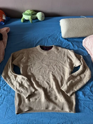 Beige stickad tröja Tommy Hilfiger - Säljer en beige stickad tröja från Tommy Hilfiger i storlek M. Tröjan har rund hals, ribbade muddar och ett litet broderat Hilfiger-logo på bröstet. Perfekt för dig som gillar klassisk och enkel stil med snygga detaljer. Tröjan stryks innan fraktning, pris går alltid att diskutera 