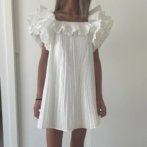 Vit plisserad kortklänning med volang - Säljer min Så fina och eftertraktad klänning från Zara!! 💓💓❤️🙏🏼stor i storleken skulle säga att den sitter mer som en S 🙏🏼💓