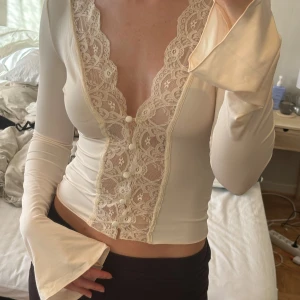 Venderby’s Pretty Luna basic top - cream - Så snygg krämvit blus från Venderby's med lång ärm, djup v-ringning och spetsdetaljer framtill. Knappar längs spetsen och utsvängda ärmslut ger en extra touch. Gjord i otroligt skön och mjuk polyesterblandning med stretch för perfekt passform. Storlek XS/S. Aldrig använd, endast testad. Kostar 399 danska kronor på hemsidan ~ 588 svenska kronor. Översta knappen sitter inte lika bra som dom andra (den kom så när jag beställde den tyvärr) men går lätt att sy fast och följer även med 2 extra knappar