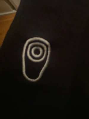 Sail Racing zip - Svart t-shirt med en vit broderad logga på bröstet som har ett cirkulärt mönster. T-shirten har klassisk passform och är gjord i mjukt bomullsmaterial. Perfekt för dig som gillar stilrena detaljer och enkel design.