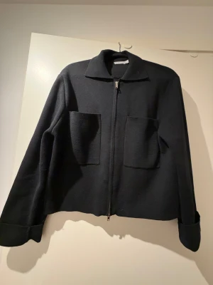 Svart overshirt med dragkedja - Stilren svart overshirt från Åhléns  med två stora fickor framtill och klassisk krage. Jackan har rak passform, långa ärmar och stängs med dragkedja. Nypris 599kr, använd 1 gång!!