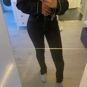 Grå svarta high waist jeans med slits - Snygga svarta jeans med hög midja och rak passform. Jeansen har en slits vid benslutet som ger en cool detalj och är tillverkade i klassiskt denimtyg. Perfekta för dig som gillar en stilren look med lite edge.