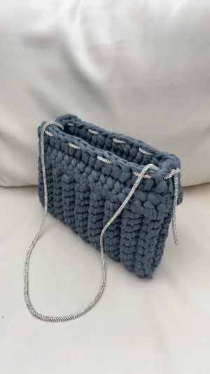 Virkad  blå axelväska med kedja - Säljer en snygg handvirkad axelväska i blå med grov struktur och silverfärgad kedja som axelrem. Perfekt för dig som gillar unika accessoarer med handgjord känsla. Väskan har rektangulär form och är både praktisk och trendig.