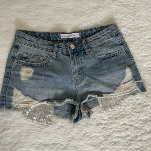 Blå denimshorts med paljettdetalj - Ett par blåa jeansshorts med paljettdetaljer, knappt använda, lite små i storleken kanske. Skriv för mått! 🫰