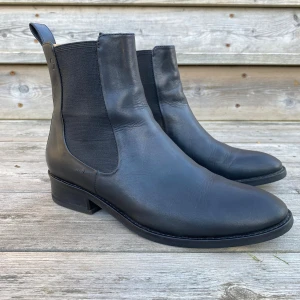 Svarta chelsea boots från Vagabond - Snygga svarta chelsea boots från Vagabond i slätt skinn med elastiska paneler på sidorna och dragflik baktill. Bootsens klassiska rundade tå och låga klack gör dem till ett stilrent val. Insidan är ljusbrun och mjuk för extra komfort.