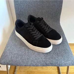 Svarta Vagabond sneakers mocka - Snygga svarta sneakers från Vagabond med ovandel i mjuk mocka och vita platta gummisulor. Klassisk rund tå och snörning framtill. Perfekt för dig som gillar stilrena och tidlösa skor med en modern touch. Storleken är att de passar 41. Sulan kan bara bytas till vilken man vill 