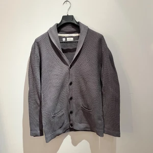 Grå kofta från PL & CO Casual Attire - Säljer en grå kofta från PL & CO Casual Attire i storlek L. Koftan har ett strukturerat stickat mönster, knappar framtill, två fickor och en bred krage. Perfekt för lager-på-lager och chill stil. Hör av er vid frågor