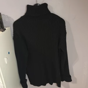 Svart ribbad polotröja från NA-KD - Svart ribbstickad något längre polotröja från NA-KD med hög krage och långa ärmar. Tröjan har en loose fit och slits i sidorna för extra detalj. Perfekt för lager-på-lager och snygg till både jeans och kjol.