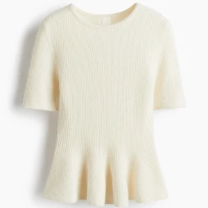Krämvit stickad topp från H&M - Säljer en krämvit stickad topp från H&M i storlek M. Toppen har korta ärmar, rund hals och en snygg volangkant nedtill som ger en cool siluett. Ribbad struktur i mjukt material som känns skönt mot huden. Perfekt för dig som gillar stilrena och trendiga plagg. Tröjan är aldrig använd.