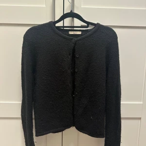 Svart kofta från Gina Tricot XS - Mysig svart kofta från Gina Tricot i storlek XS. Koftan har rund hals, långa ärmar och knäppning med tre knappar framtill. Materialet är fluffigt och stickat, vilket gör den extra skön och snygg att ha på sig. Perfekt att slänga över en topp för en chill look.