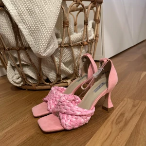 Rosa klackar med flätad rem och klack - Säljer ett par trendiga rosa klackar från nelly med fyrkantig tå, flätad rem över foten och snygg klack. Skorna har ankelrem med spänne och är tillverkade i ett mjukt material som känns lyxigt. Perfekta för att lyfta din outfit med en poppig färg.