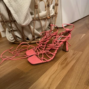 Rosa sandaler med snörning från NA-KD - Säljer ett par trendiga rosa sandaler från NA-KD med fyrkantig tå, höga klackar och långa snören som kan lindas runt benet. Skorna har öppen tå och är tillverkade i syntetmaterial. Perfekta för att lyfta vilken outfit som helst.