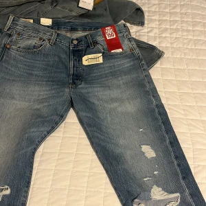 Levi's 501 jeans ljusblå 34x34 - Ljusblå Levi's 501 jeans med klassisk rak passform och slitna detaljer på benen för en cool vintagekänsla. Jeansen är tillverkade i 100% bomull och har fem fickor, knappgylf och ikonisk röd Levi's-tag bak. Perfekt för dig som gillar tidlös streetstil.