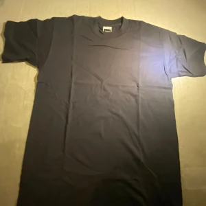 Svart t-shirt från Fruit of the Loom - En klassisk svart t-shirt från Fruit of the Loom, modell Screen Stars Xtra-Premium T. T-shirten är i 100% bomull, har rund hals och korta ärmar. Perfekt basic-plagg med normal passform och mjukt material.